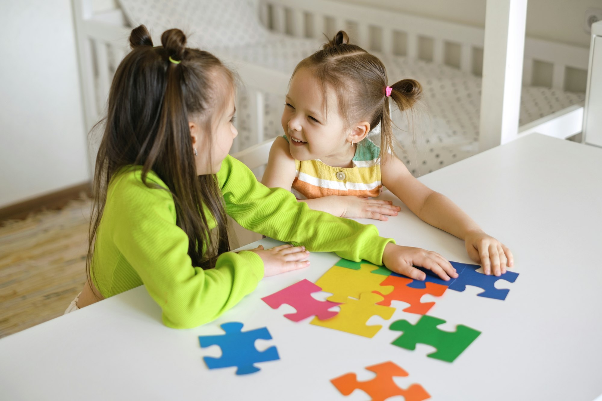 Funny girls collect puzzles together at the table in the children's room.