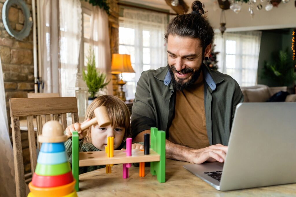 Multi-tasking freelance and fatherhood concept. Working single father with child and laptop computer